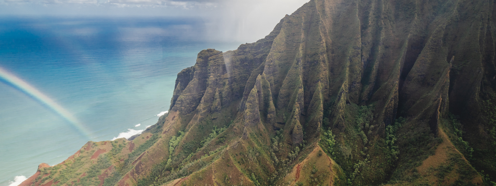 The file shows a stunning Hawaiian mountain landscape. Lush green mountains rise under a bright blue sky, with a vivid rainbow arching over them. In the background, the deep blue ocean stretches to the horizon, completing the peaceful tropical scene.