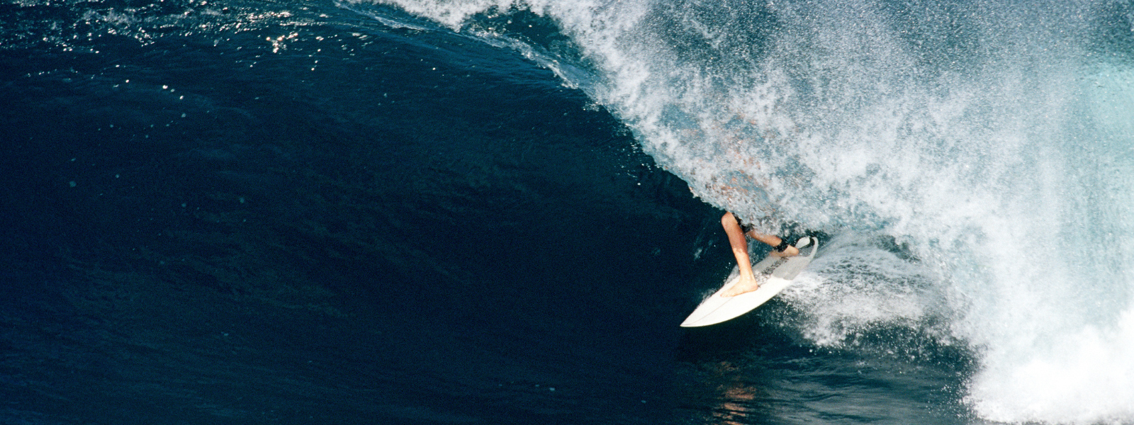 This image shows a man riding a large wave while surfing. The surfer is positioned mid-action on the wave, and demonstrating skill and balance. The ocean is turbulent with frothy whitecaps, capturing the dynamic movement of the scene.