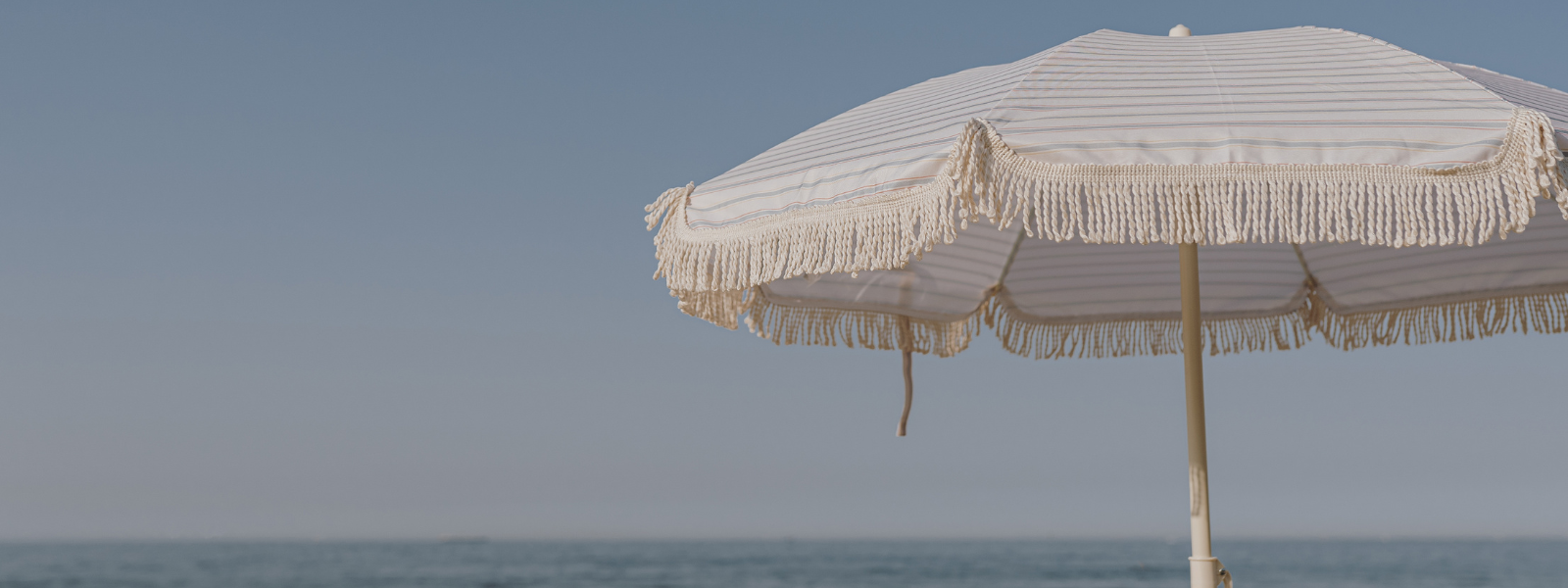  colorful umbrella shades a sandy beach, with gentle waves in the background. The umbrella is striped with bright colors, and the scene conveys a relaxing, sunny day by the sea.